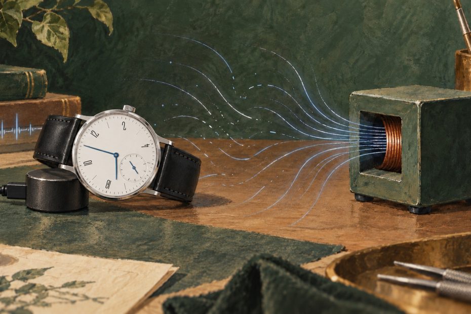 Illustration einer seitlich liegenden Tangomat-ähnlichen Uhr mit weißem Zifferblatt, blauen Zeigern und kleiner Sekunde bei sechs neben Zeitwaage und Entmagnetisierer.